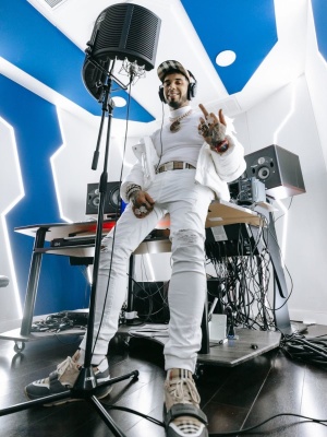 Anuel Wearing A Burberry Beige Check Hat And Belt With A Moncler Puffer Richard Mille Watch And Burberry Sneakers