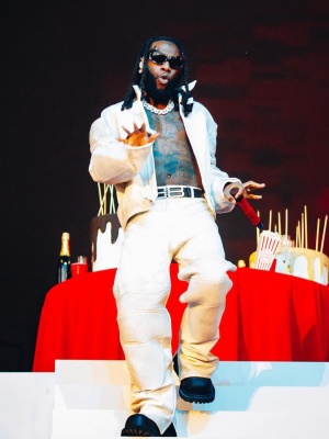 Burna Boy Wearing Balenciaga Gotham Sunglasses With A White Leather Jacket And Pants And Boots