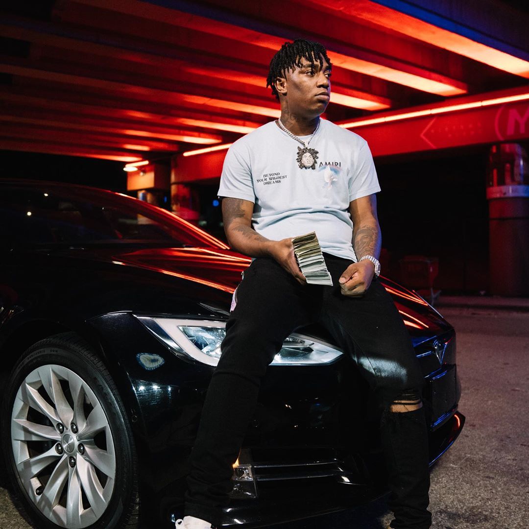 Fredo Bang Chills On Top Of His Telsa In an Amiri Dove Tee & Watercolor Jeans