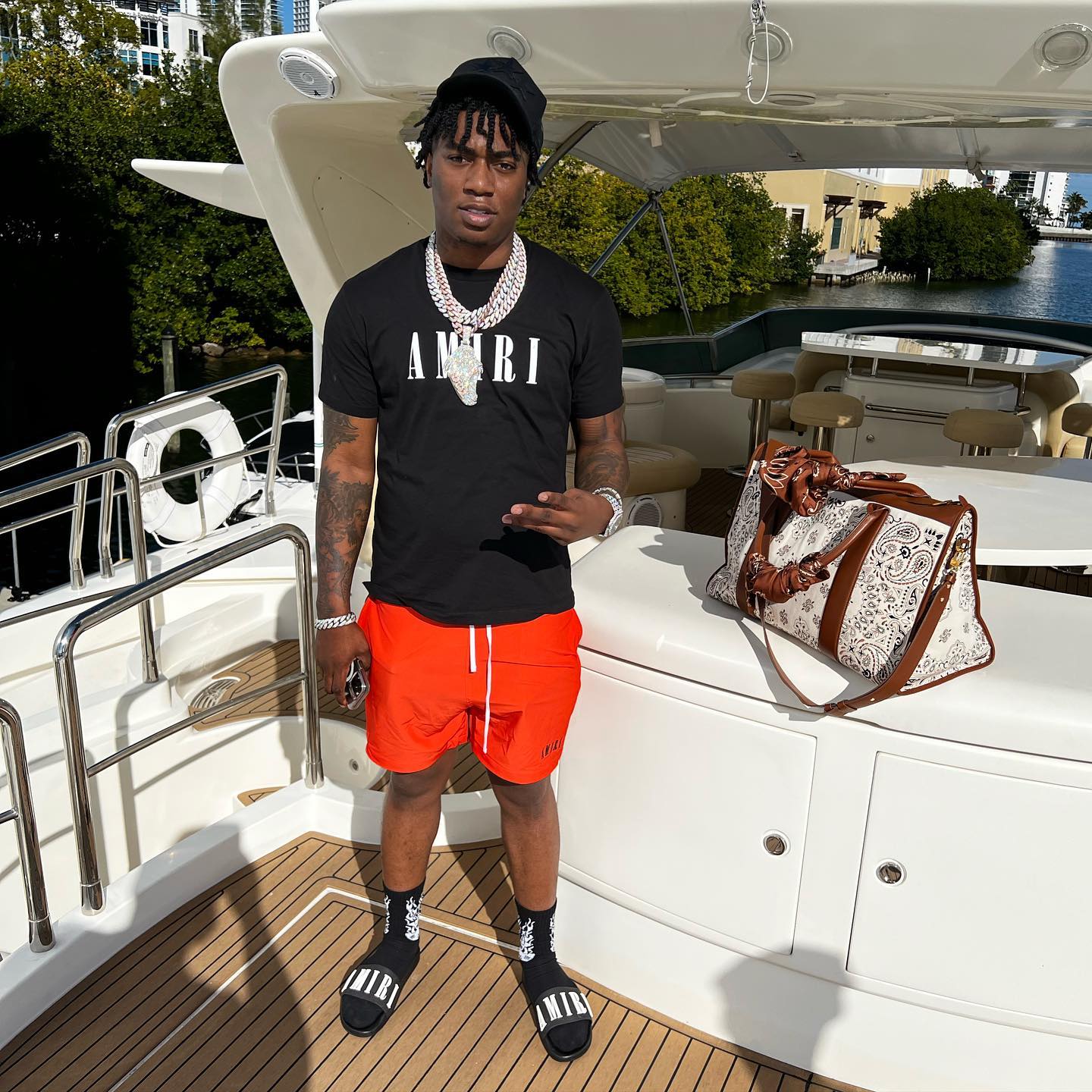 Fredo Bang Enjoying Yacht Life In a Full Amiri Hat, T-Shirt, Shorts, Socks, & Sandals Outfit