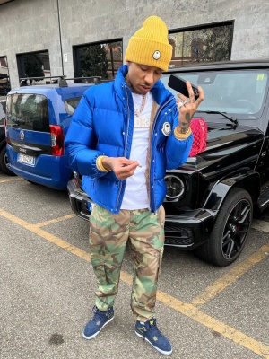 Fredo Wearing A Yellow Moncler X Palm Angels Beanie And Blue Jacket With Camo Pans And Jordan Sneakers