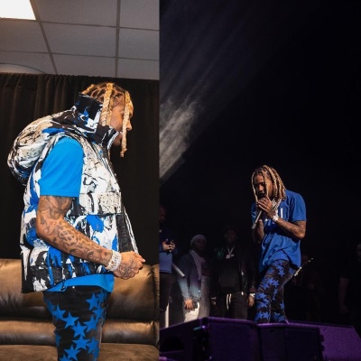 Lil Durk Wearing An Amiri Blue Paint Splatter Puffer Vest With A White Core Logo Tee And Amiri X Chemist Black And Blue Star Jeans