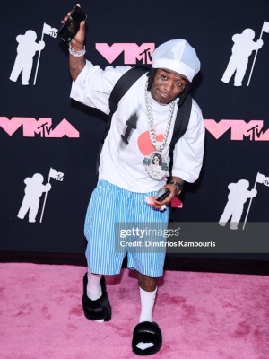Lil Uzi Vert Wearing A Balenciaga Tee And Blue Striped Shorts And Black Fuzzy Slippers