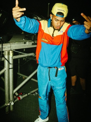 Myke Towers Wearing A Mitchell Ness Hat With Polo Ralph Lauren Colorblock Jacket And Bmx Pants