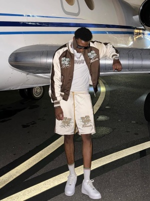 Rob49 Wearing A Rhude Brown Logo Jacket And Palms Print Shorts With Nike Air Force 1 Sneakers