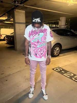 Skilla Baby Wearing A Hellstar Beanie And Neon Tee With Amiri Jeans And Louboutin Sneakers