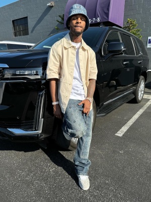 Toosii Wearing A Lvxyk Bucket Hat With A Cream Shirt And Jeans And Striped Lv Trainer Sneakers