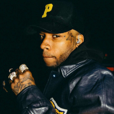 Tory Lanez Wearing A Black And Yellow Leather Varisty Jacket And A Black Hat With A Yellow Letter P