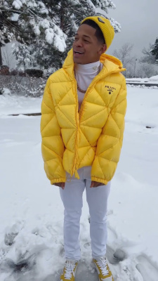 Yk Osiris Wearing A Prada Yellow Beanie And Down Jacket With A White Turleneck And Yellow Sneakers